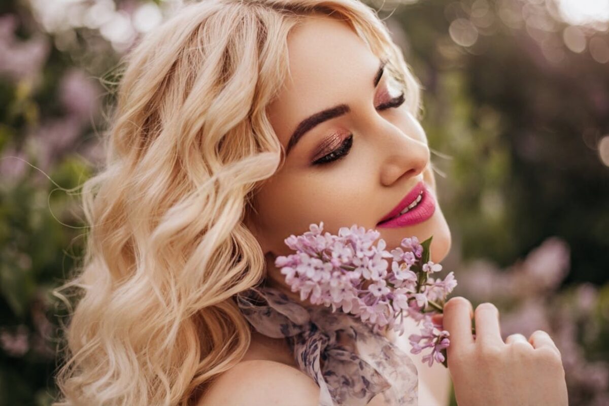 Smiling blonde woman with flowers enjoying spring outdoors, highlighting beauty and floral elegance.
