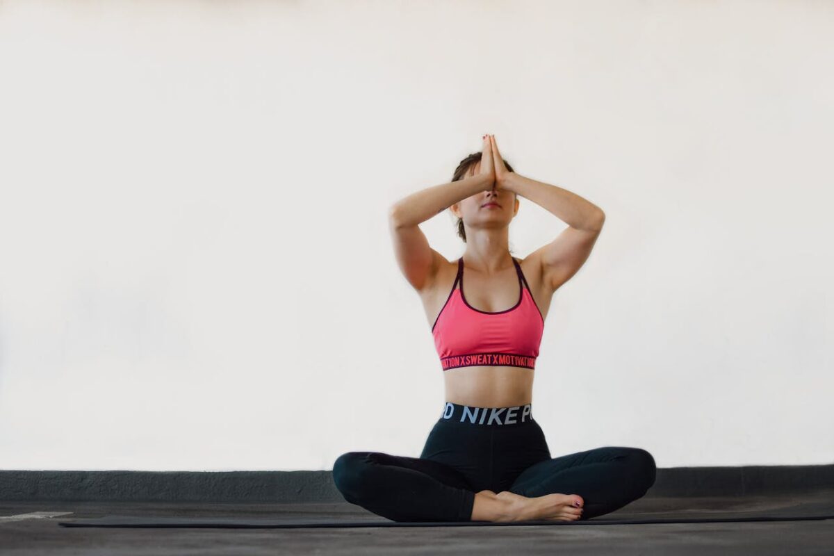 A woman in activewear practices yoga, sitting in a meditative pose indoors, creating a calm atmosphere.